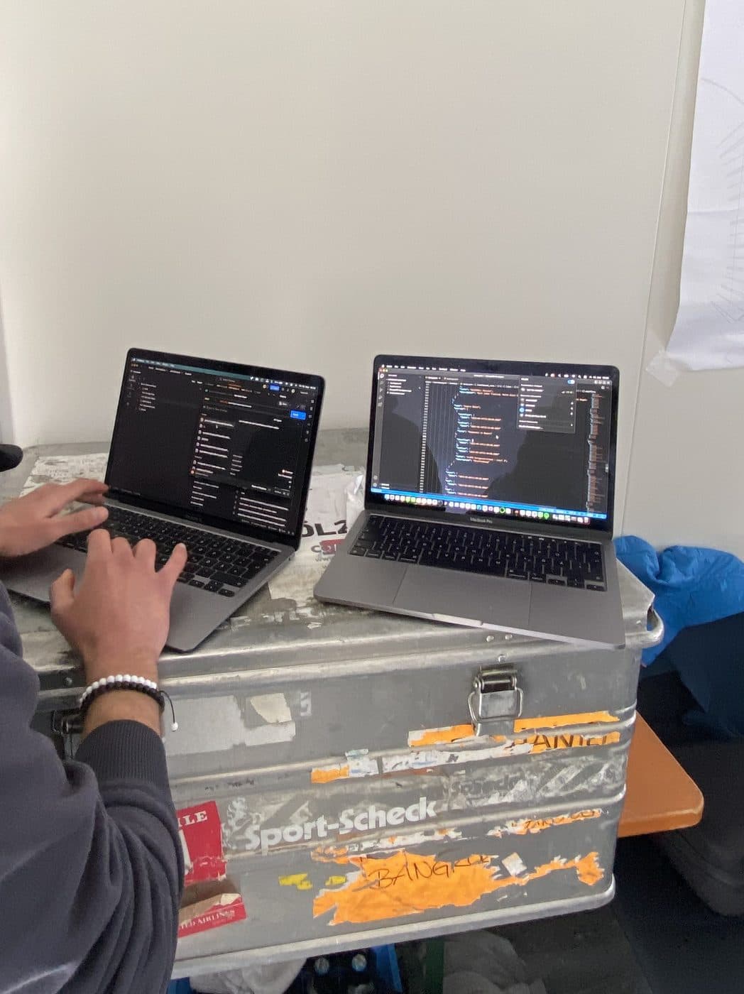 Hände auf zwei Laptops mit Code, die auf einer Transportkiste stehen