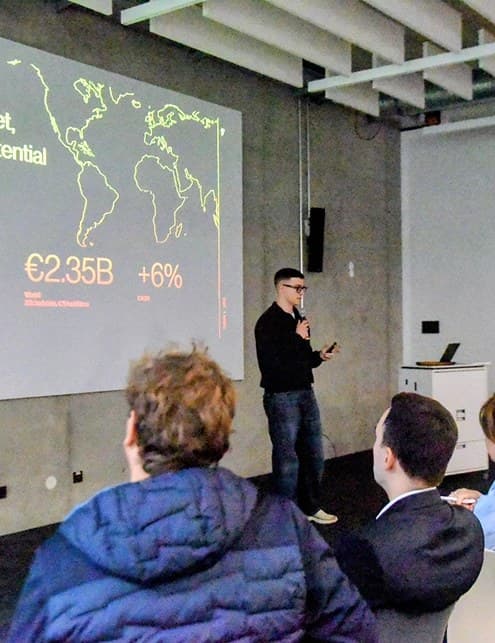 Teammitglied pitcht vor Publikum, auf der Leinwand eine Weltkarte mit Marktzahlen